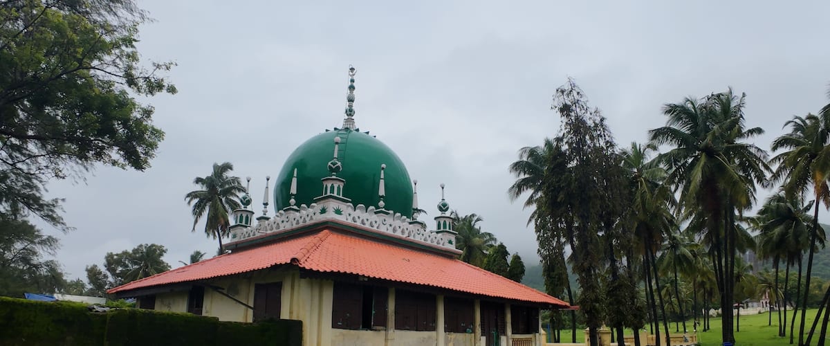 A green-domed building with a red roof, surrounded by palm trees and greenery.
