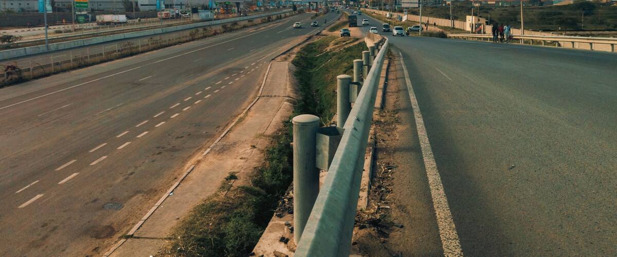 Une autoroute à plusieurs voies, séparée par une barrière centrale, avec des grues de construction et des bâtiments en arrière-plan.