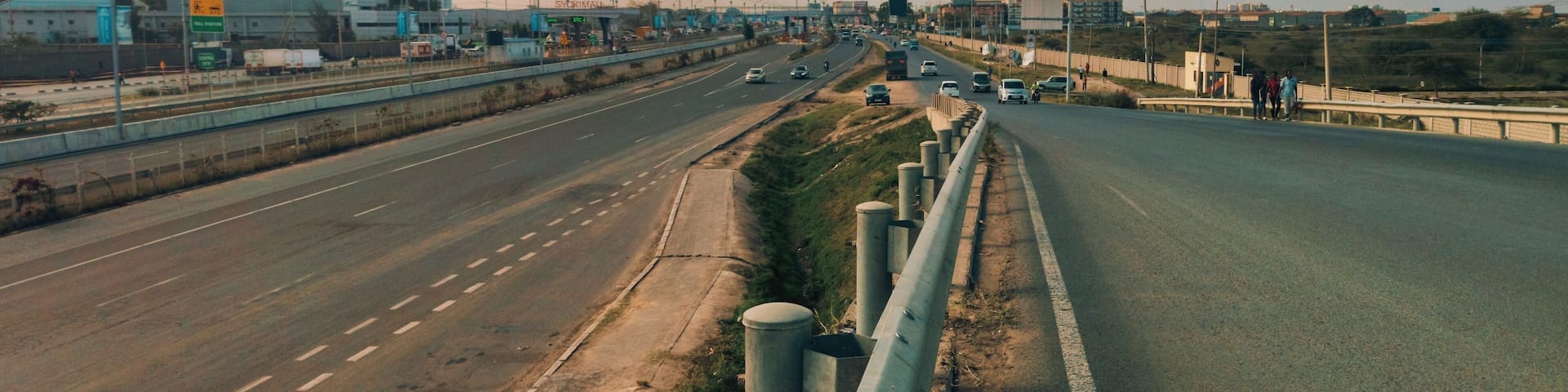 A multi-lane highway with a median barrier, construction cranes, and buildings in the background.