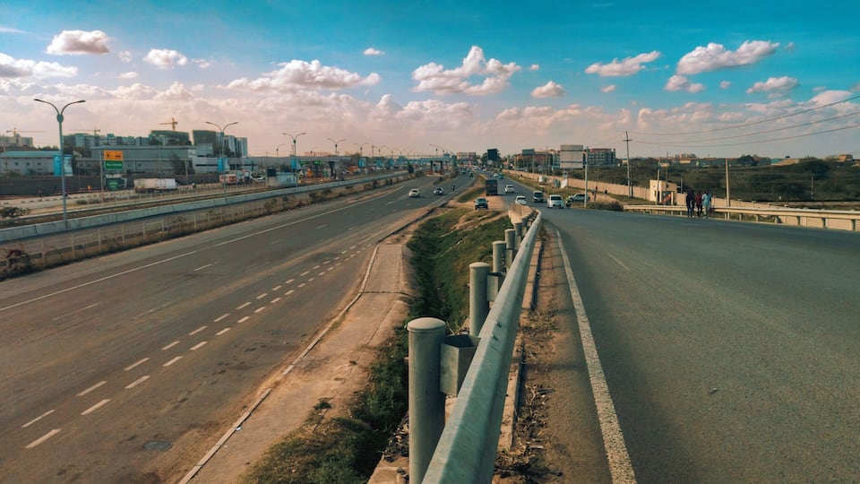 A multi-lane highway with a median barrier, construction cranes, and buildings in the background.