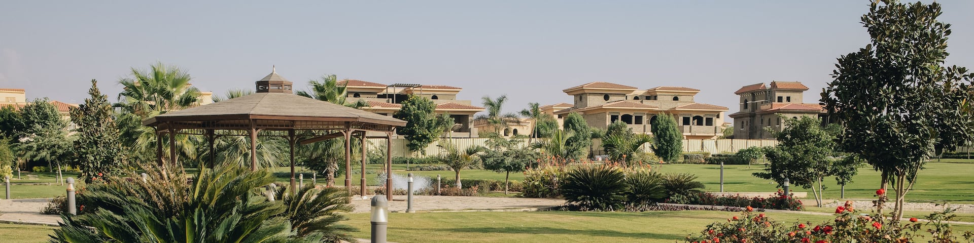 A landscaped garden with a pathway, red flowers, and buildings in the background.