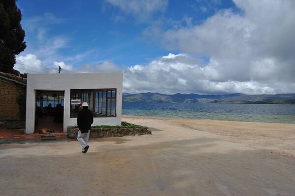 A coastal area with a white building, a person walking, and mountains in the background.