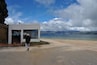 A coastal area with a white building, a person walking, and mountains in the background.