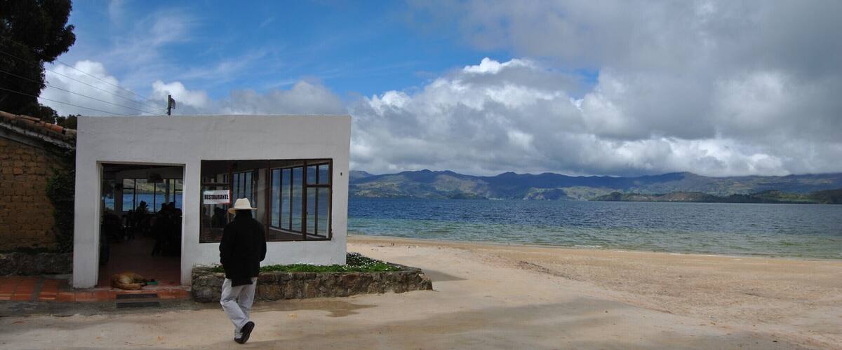 A coastal area with a white building, a person walking, and mountains in the background.