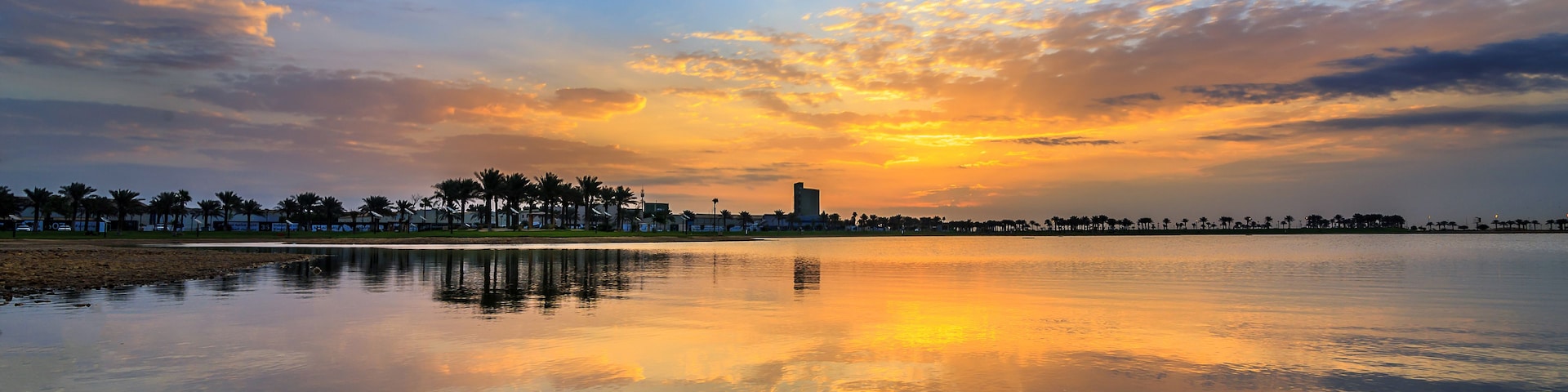 Um pôr do sol sobre águas calmas, com o horizonte da cidade ao fundo.
