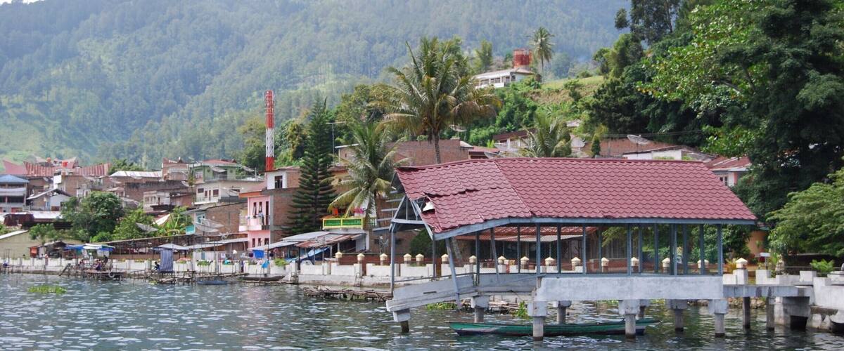 A riverside town with a bridge, boats, and a mountain backdrop.