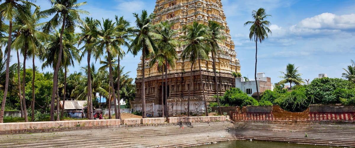 A tall, intricately carved temple with a surrounding water body and palm trees.