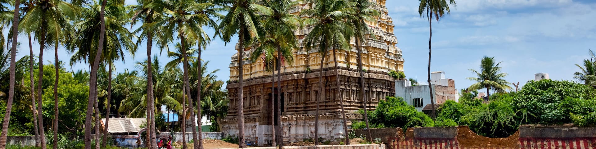 A tall, intricately carved temple with a surrounding water body and palm trees.