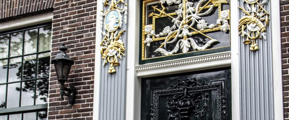 A black ornate door with gold accents and a plaque reading "TKoopmanshuys d'Mol 1795".