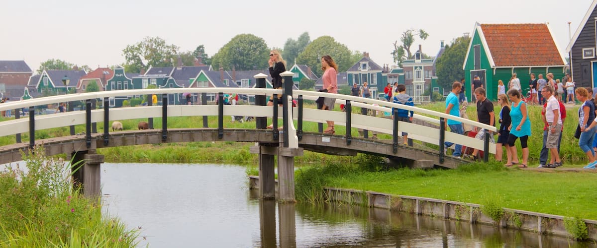 A wooden bridge over a canal with people on it and houses in the background.