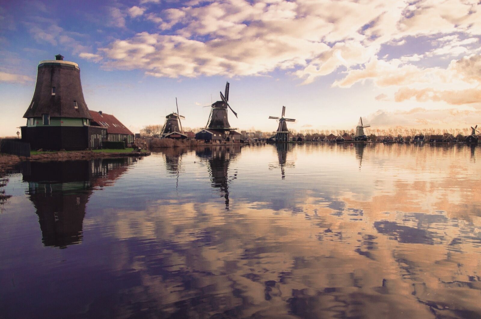 Un río tranquilo con molinos de viento y una torre reflejándose en el agua.