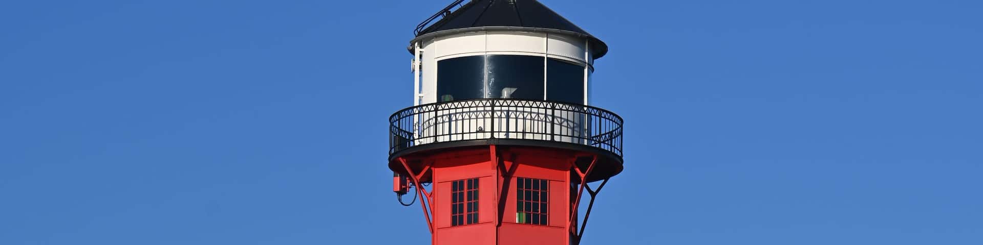 A tall red and white lighthouse with a black top, set against a clear blue sky.