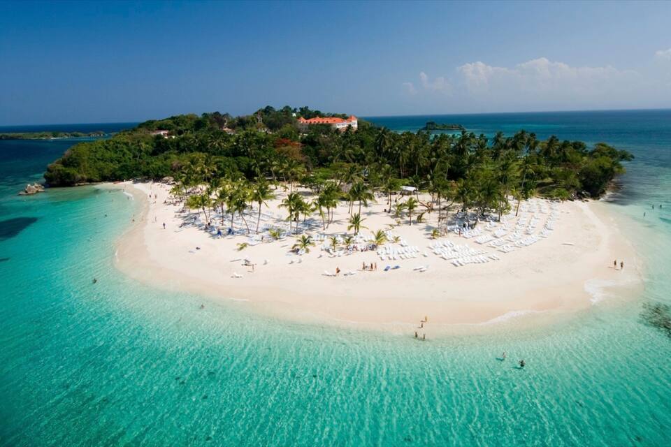An aerial view of a tropical island with a white sandy beach, clear turquoise waters, and lush greenery.