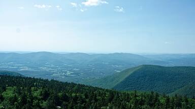 A mountainous landscape with dense forests and distant valleys under a clear sky.