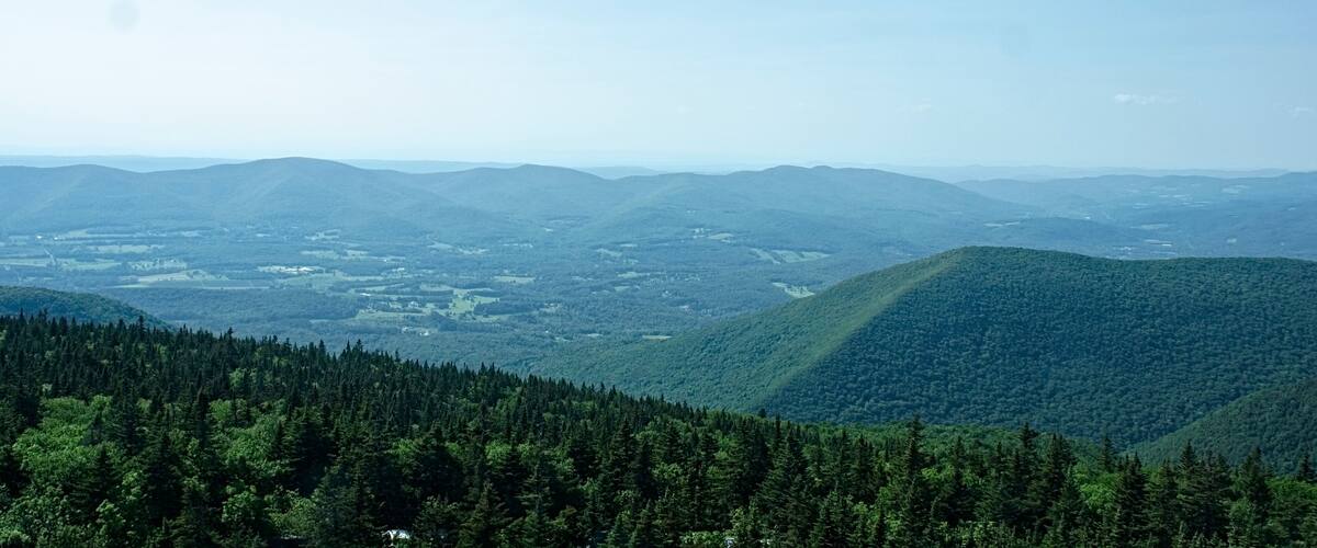 A mountainous landscape with dense forests and distant valleys under a clear sky.