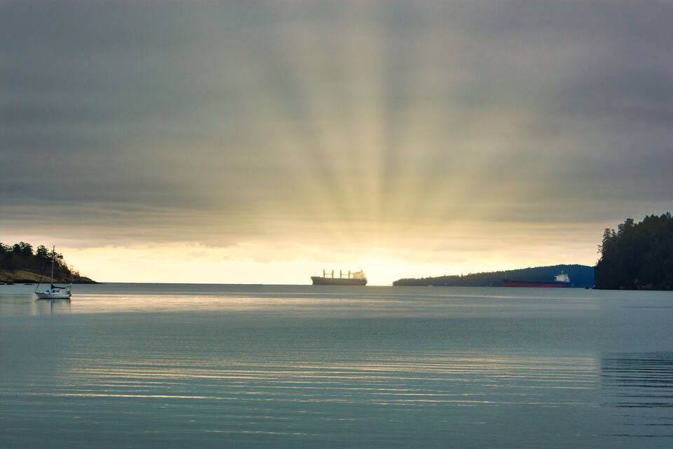 A calm body of water with a small boat and a large ship in the distance, under a cloudy sky.