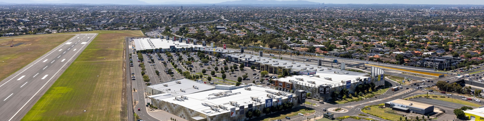 An industrial area with large buildings, a highway, and a residential neighborhood in the background.