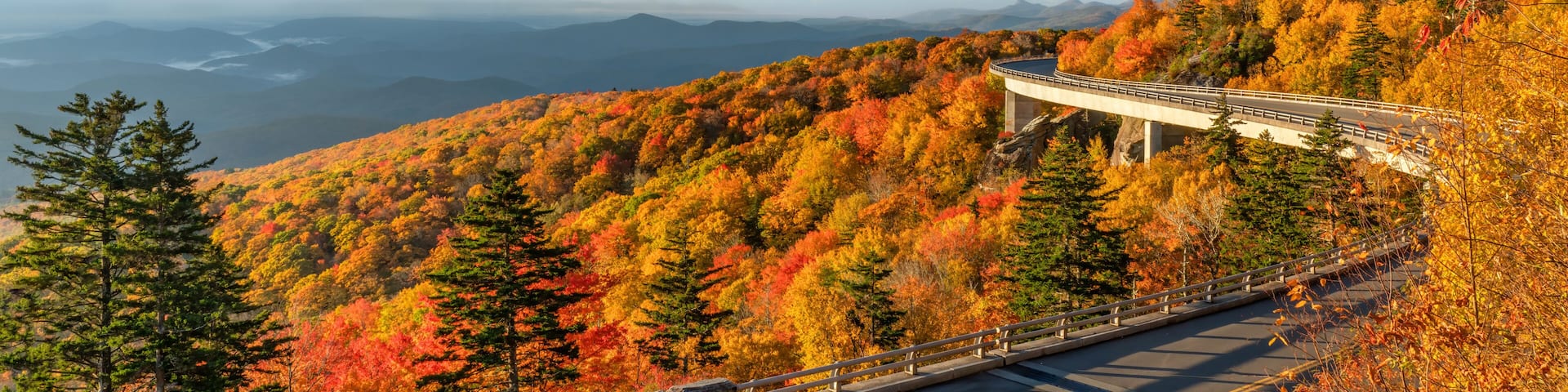 A scenic overlook with autumn foliage, a winding road, and a bridge.