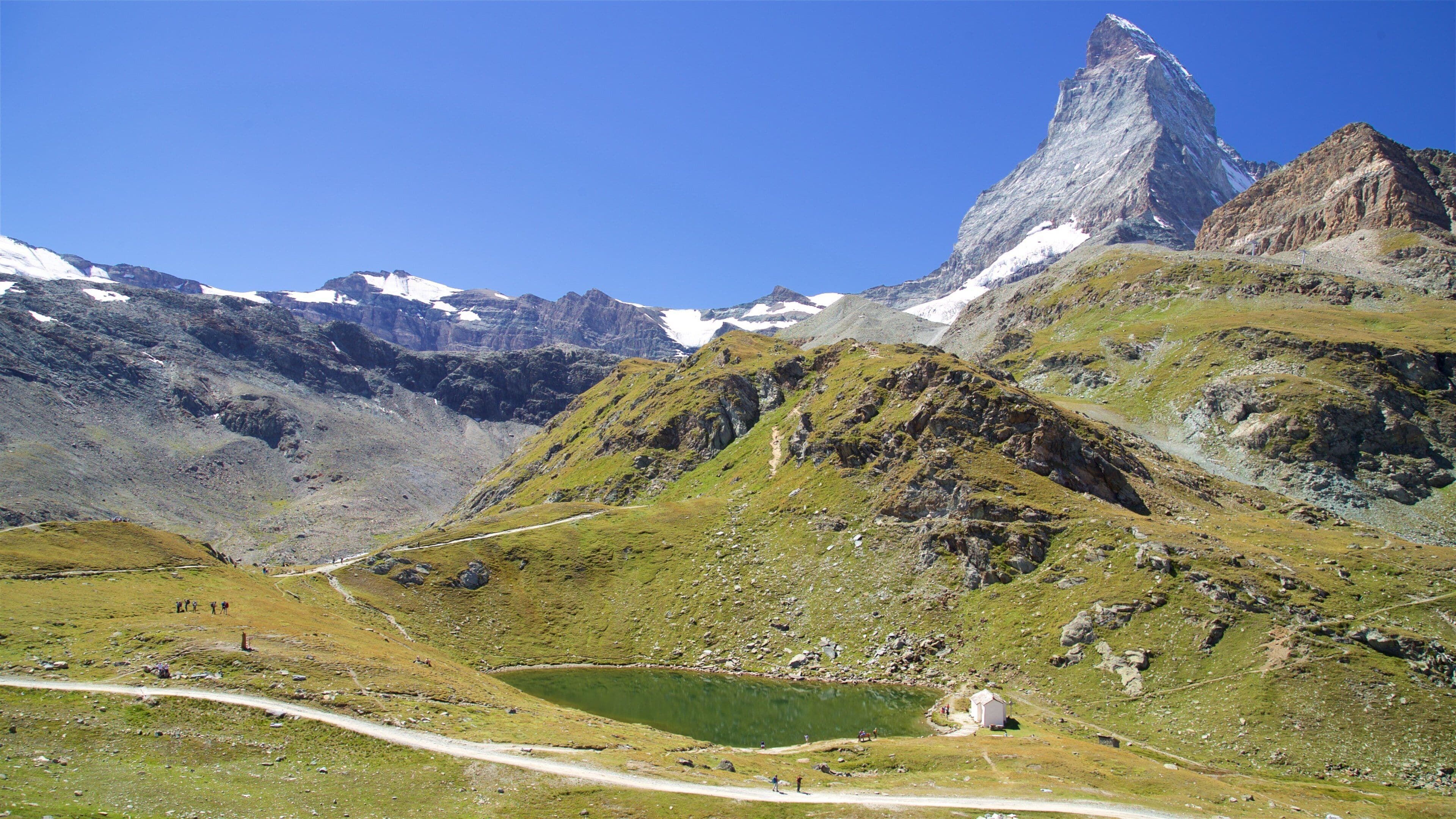 A mountainous landscape with a prominent peak, a small lake, and a trail.