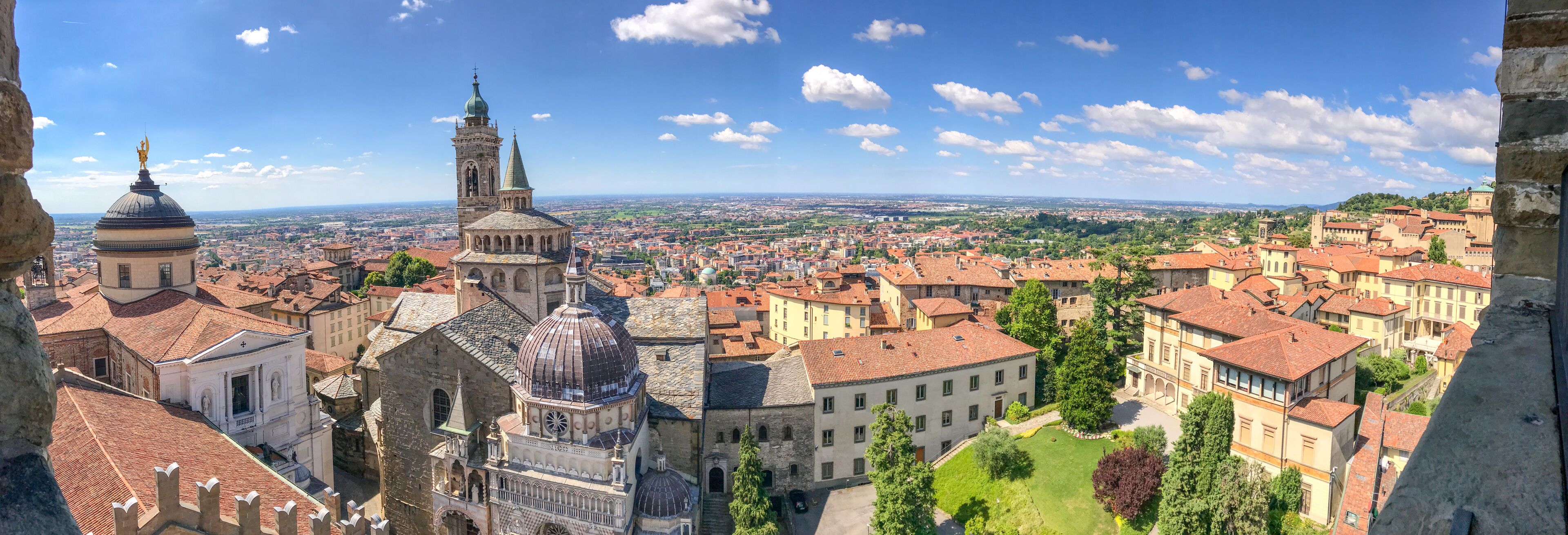 A panoramic view of a historic city with prominent domed and spire-topped buildings, a cathedral, and a distant green landscape.