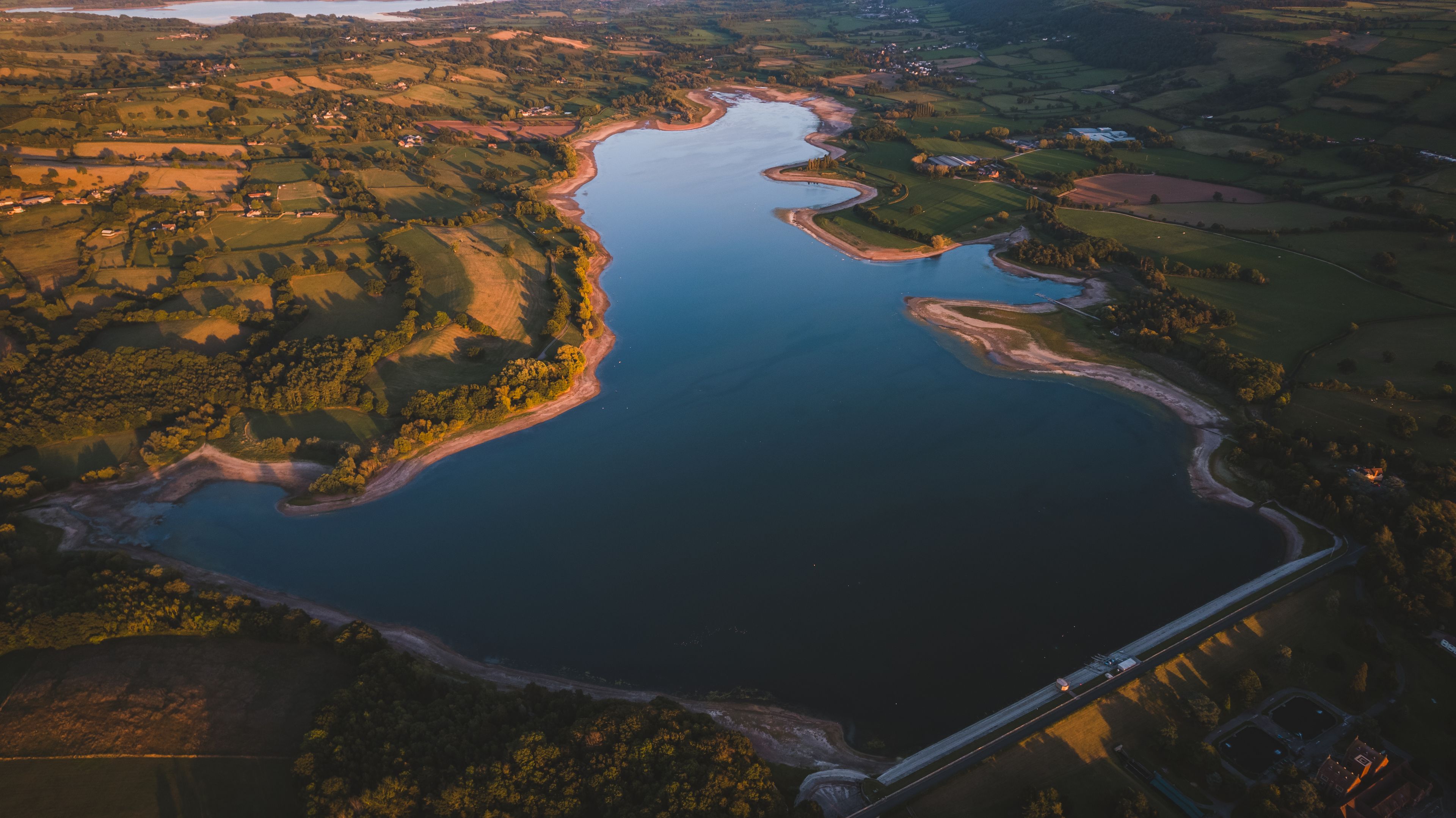 Vista aèria d'un llac gran envoltat de camps i un pont.