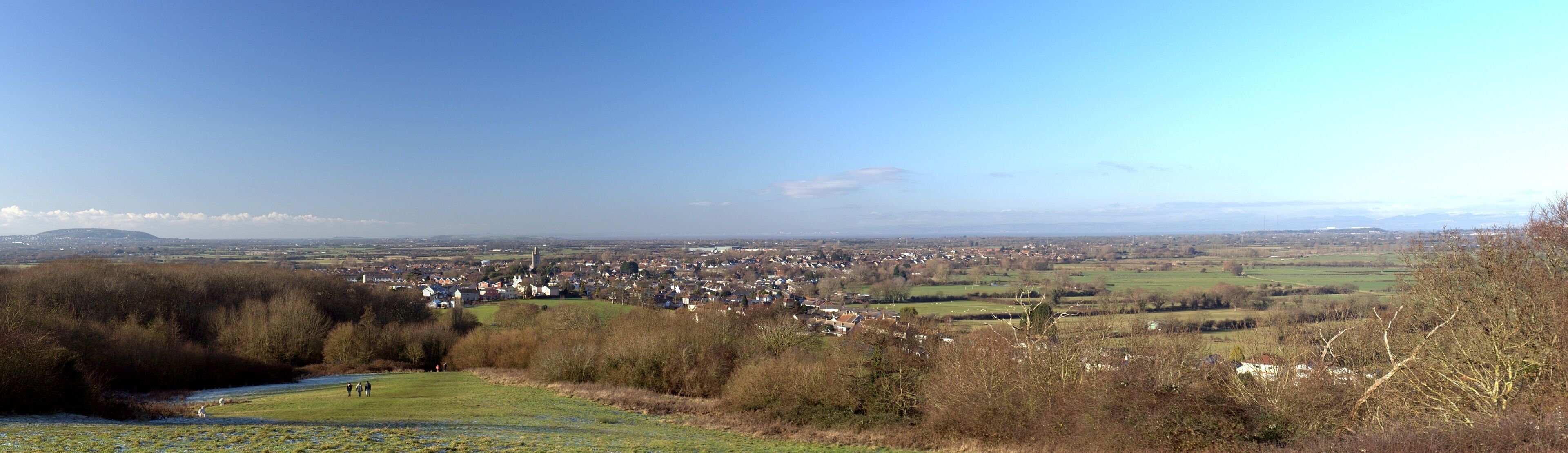 A town nestled in a valley with a river in the foreground and a clear blue sky above.