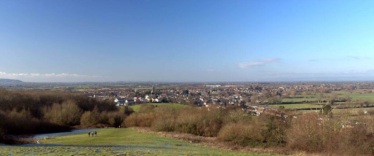A town nestled in a valley with a river in the foreground and a clear blue sky above.