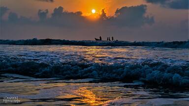 Un coucher de soleil sur l’océan, avec des vagues et un bateau où se trouvent des personnes, visibles au loin.