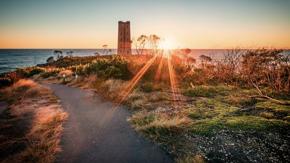 A coastal path with a tower, sunset, and vegetation.
