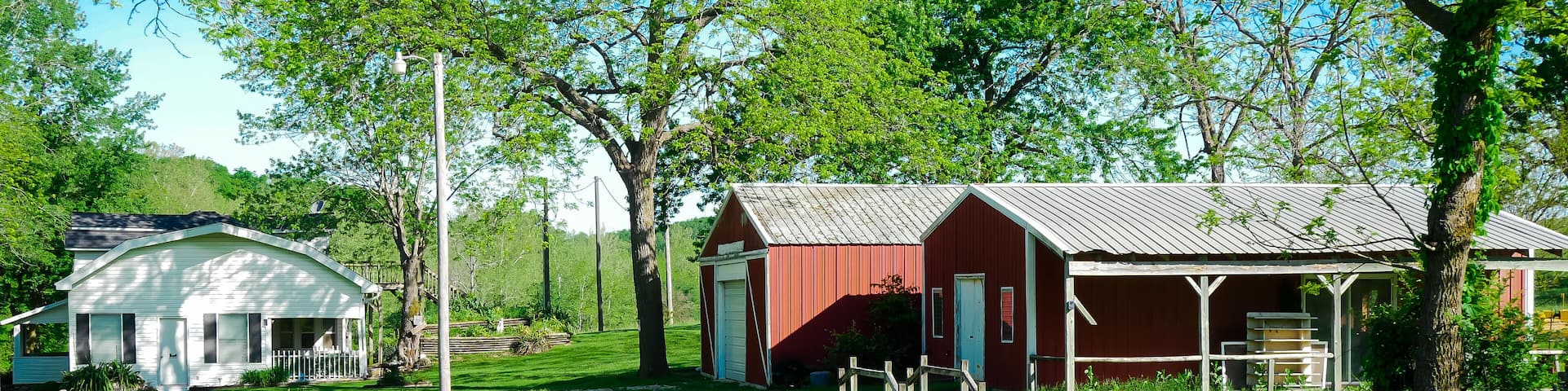 Red barn farmhouse on large acre lot farmland in Mansfield Missouri, grassy lawn and lush greenery trees, scenic peaceful agriculture town at agro-town agglomeration rural environment farmstead
