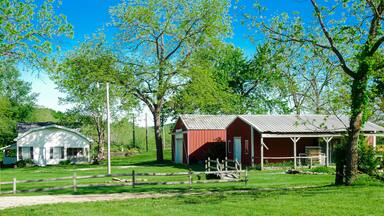 Red barn farmhouse on large acre lot farmland in Mansfield Missouri, grassy lawn and lush greenery trees, scenic peaceful agriculture town at agro-town agglomeration rural environment farmstead