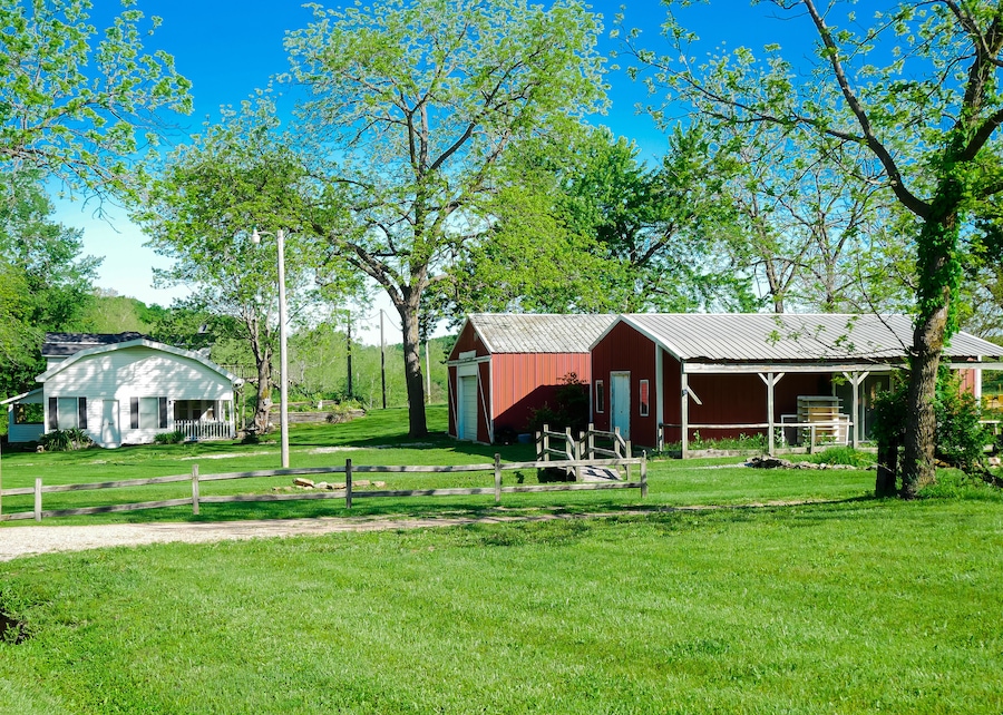 Red barn farmhouse on large acre lot farmland in Mansfield Missouri, grassy lawn and lush greenery trees, scenic peaceful agriculture town at agro-town agglomeration rural environment farmstead