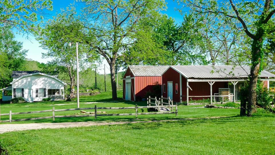 Red barn farmhouse on large acre lot farmland in Mansfield Missouri, grassy lawn and lush greenery trees, scenic peaceful agriculture town at agro-town agglomeration rural environment farmstead
