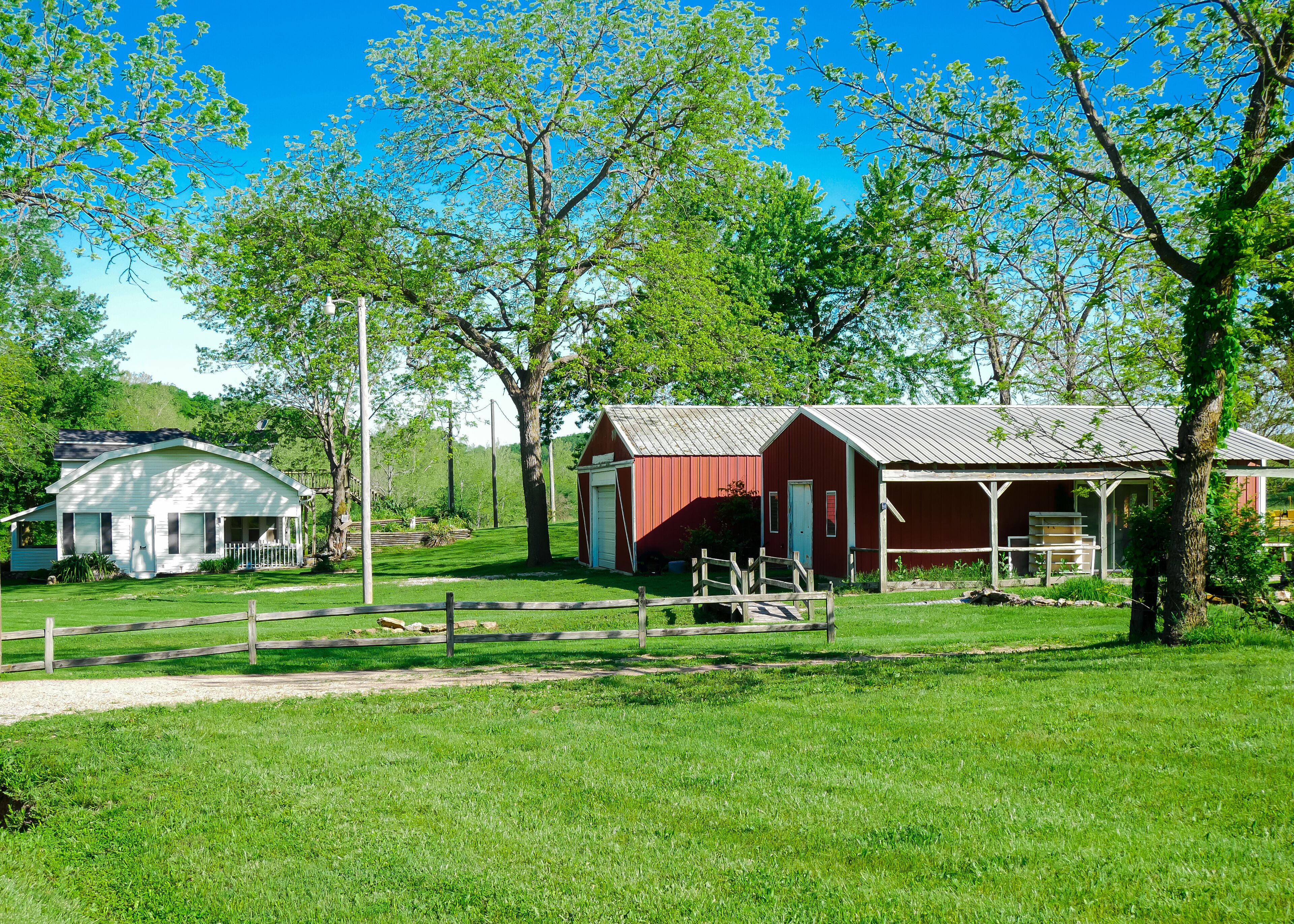 A rural landscape with a white house, a red barn, and a covered porch.