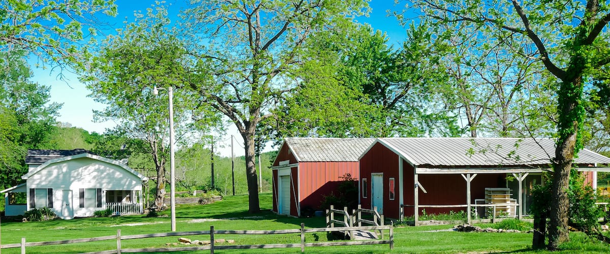 A rural landscape with a white house, a red barn, and a covered porch.