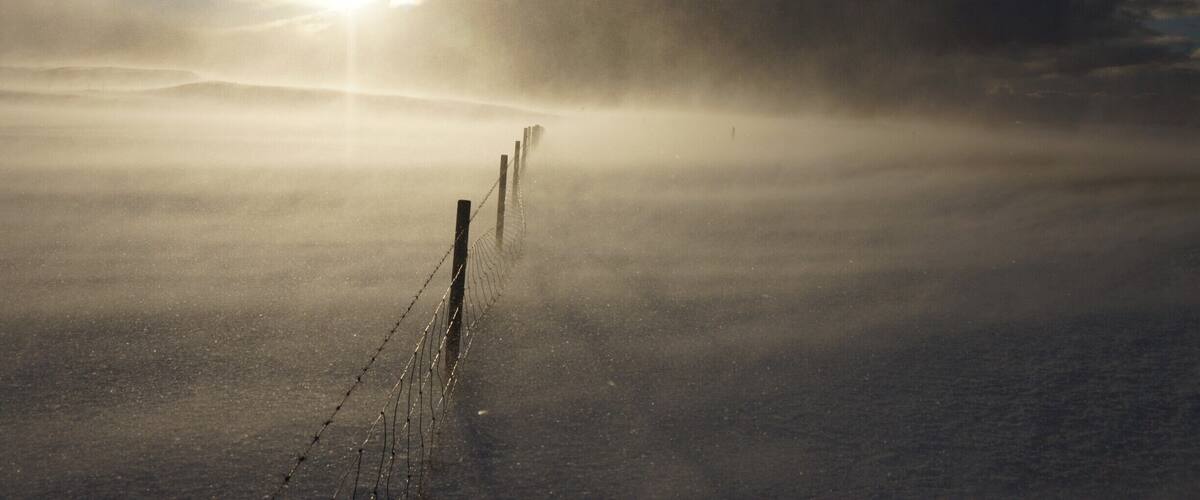 A foggy landscape with a fence and a sun peeking through the clouds.