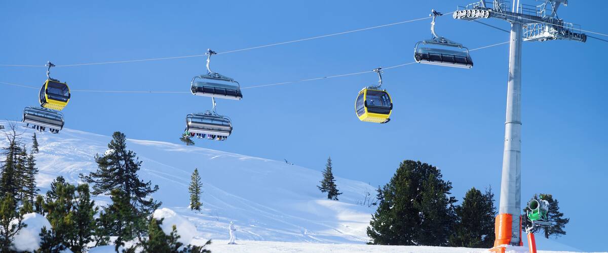 A ski lift with gondolas ascending a snowy slope, surrounded by evergreen trees.