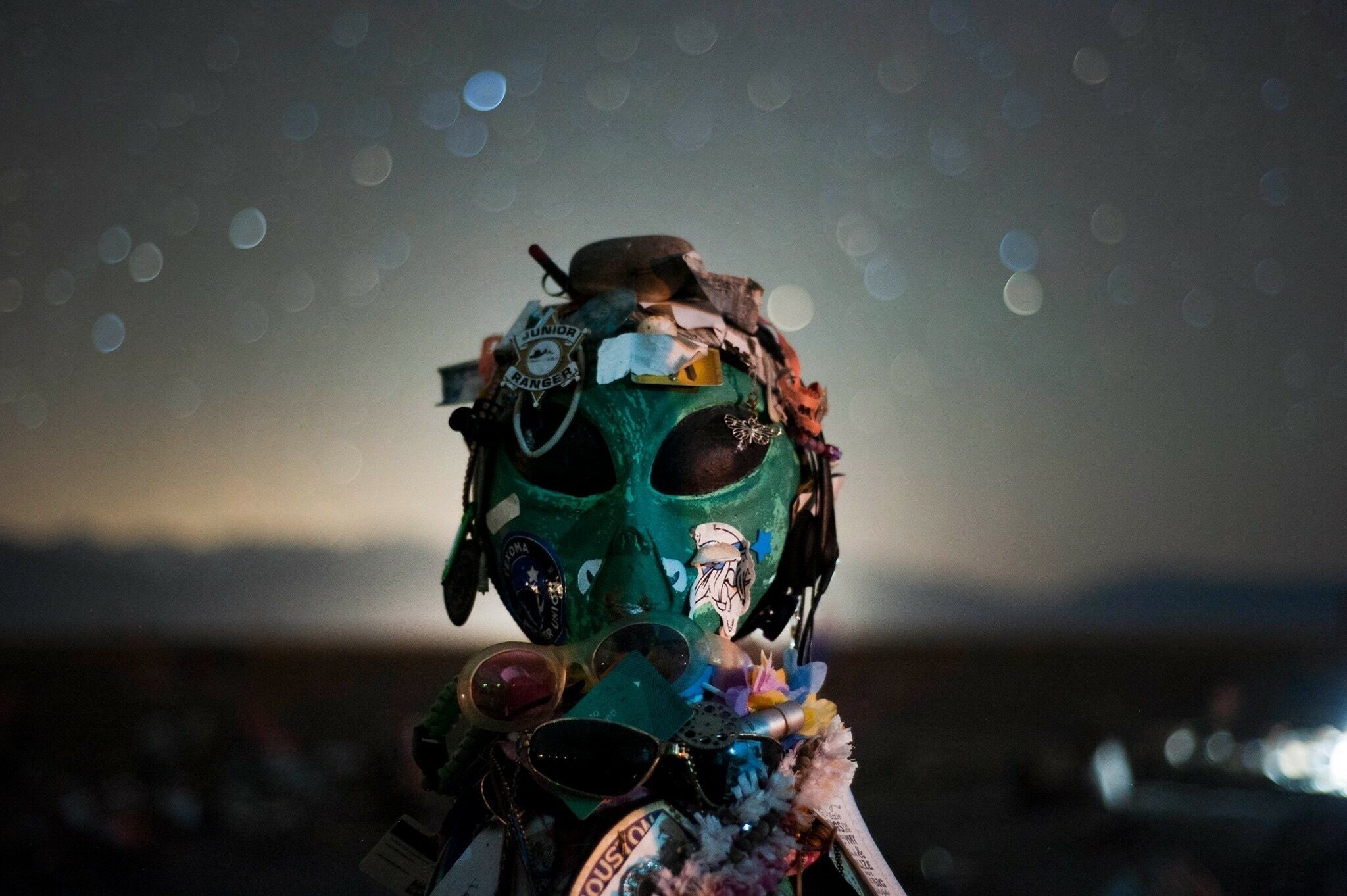A person wearing a green mask with various stickers and accessories.