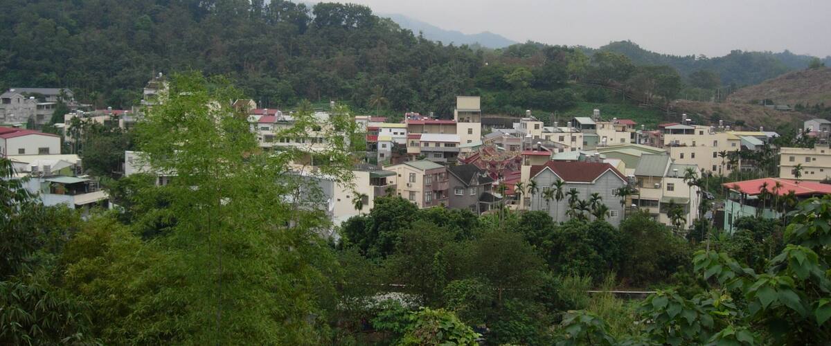 A town nestled in a valley with buildings surrounded by lush greenery and hills in the background.