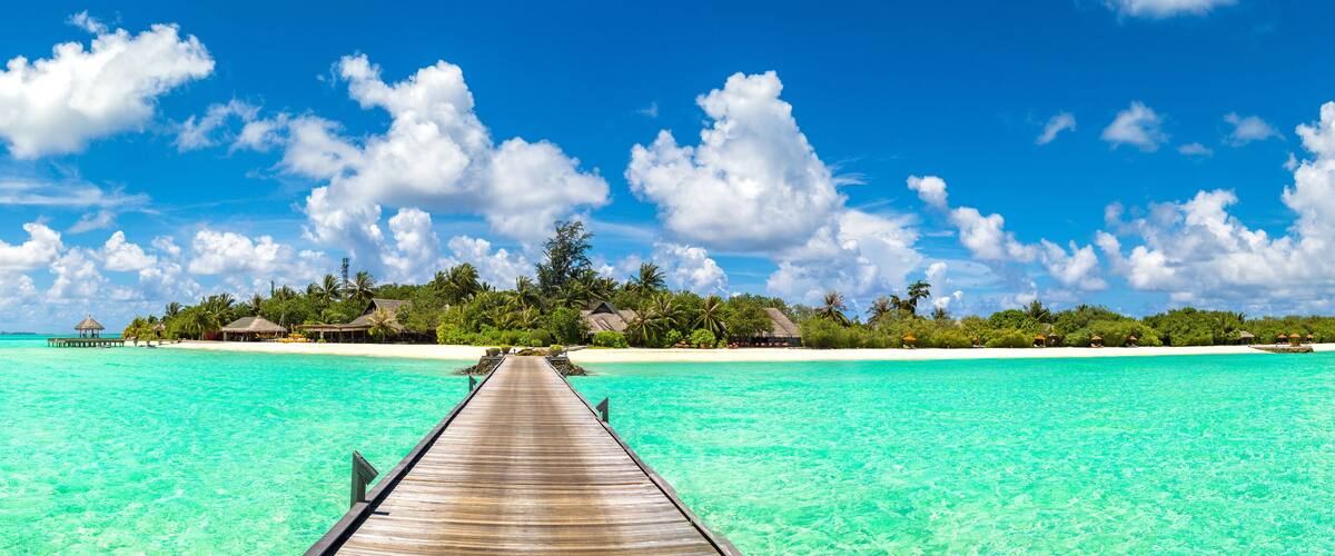 A wooden pier leading to a tropical island with clear turquoise waters and white sandy beaches.