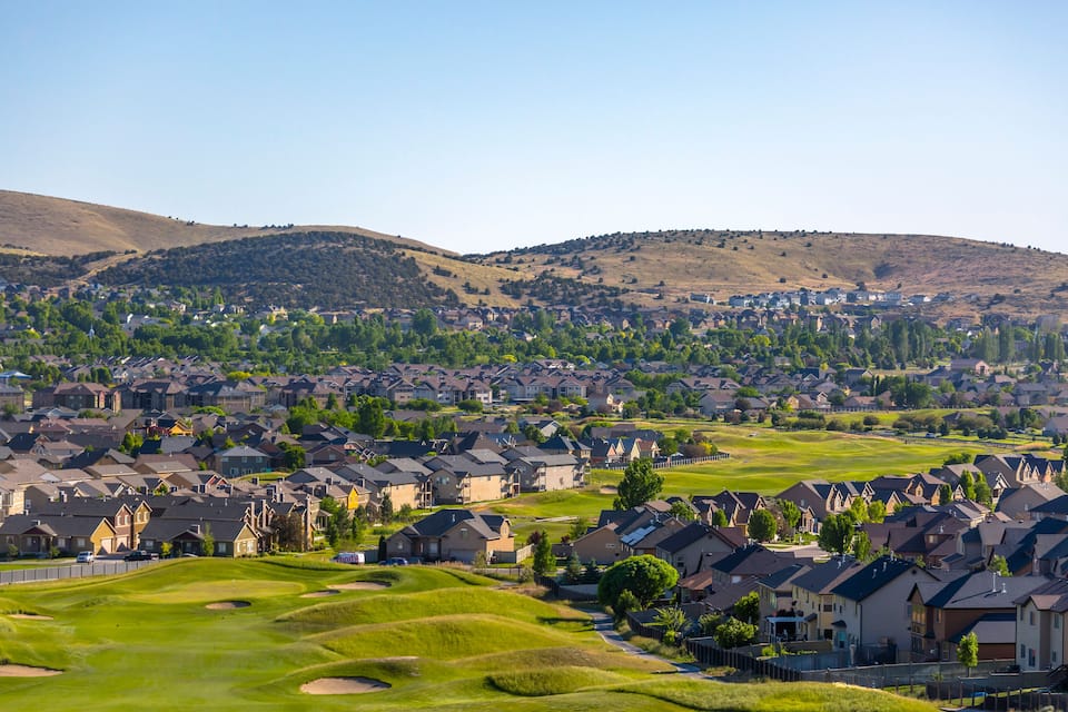 A suburban neighborhood with houses, green lawns, and rolling hills in the background.