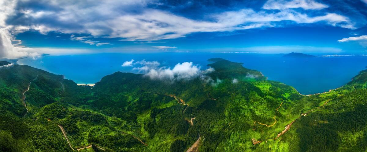 A lush green mountain range with winding roads and a clear blue sky.