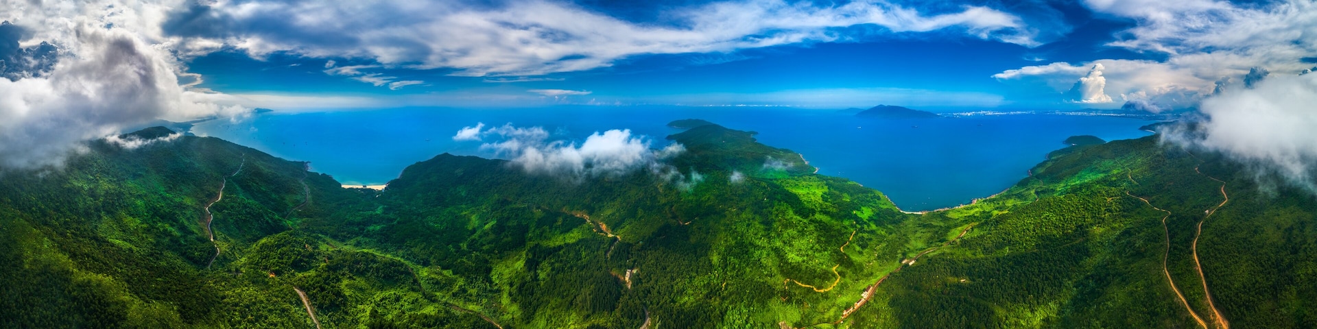 A lush green mountain range with winding roads and a clear blue sky.