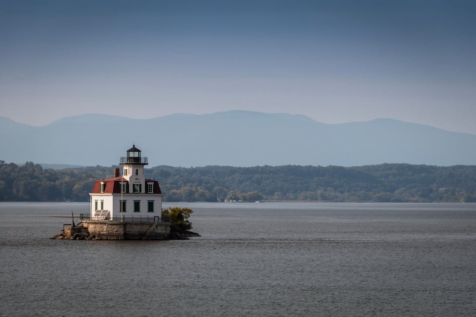 Um farol numa pequena ilha em um lago calmo, rodeado por montanhas.