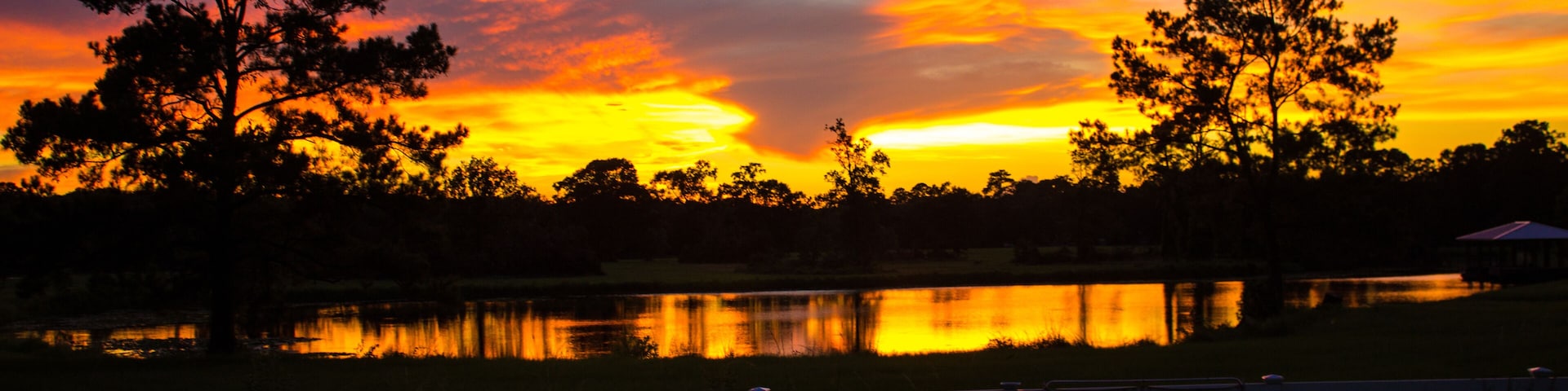 A sunset over a lake with trees silhouetted against a colorful sky.