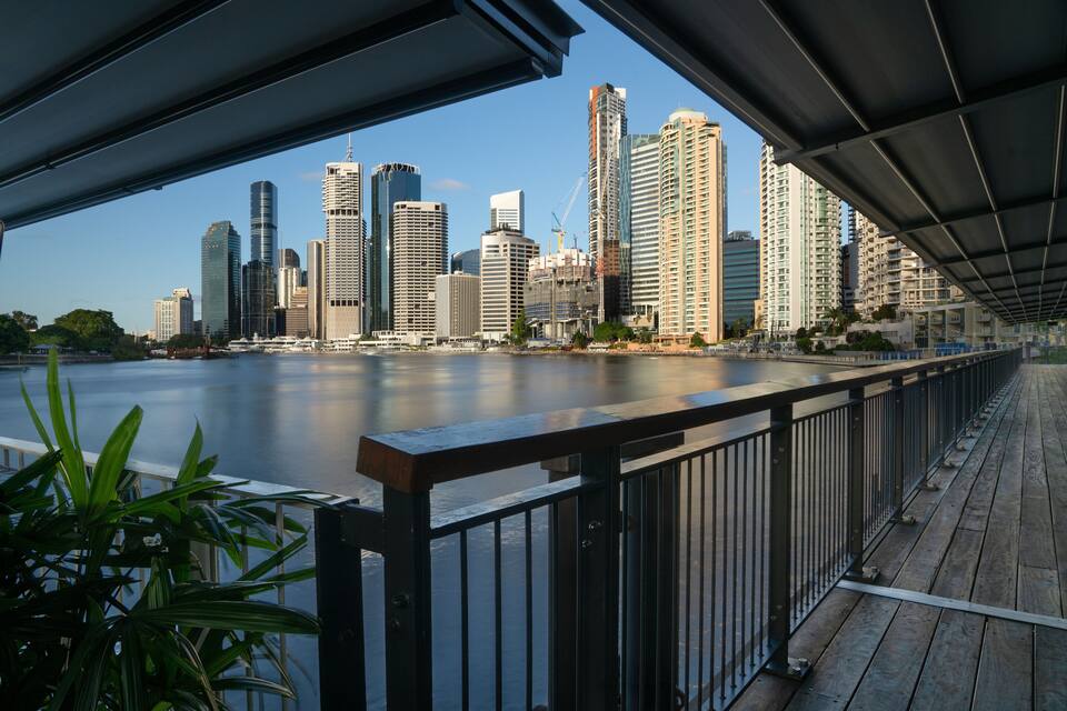 A waterfront promenade with a view of a city skyline and a river.