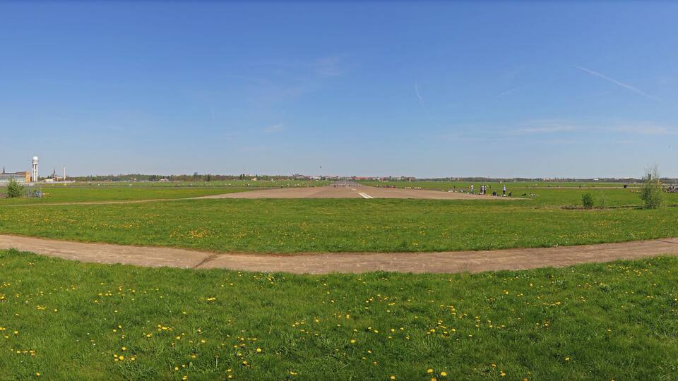 A grassy field with a dirt path, a water tower, and a clear blue sky.