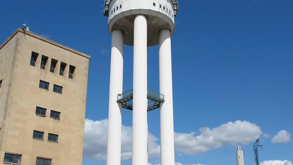 A large water tower with a dome and four supporting columns, adjacent to a beige building with multiple windows.