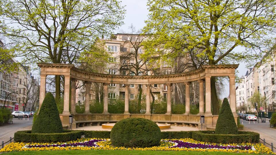 A classical pavilion with columns, surrounded by manicured gardens and trees.
