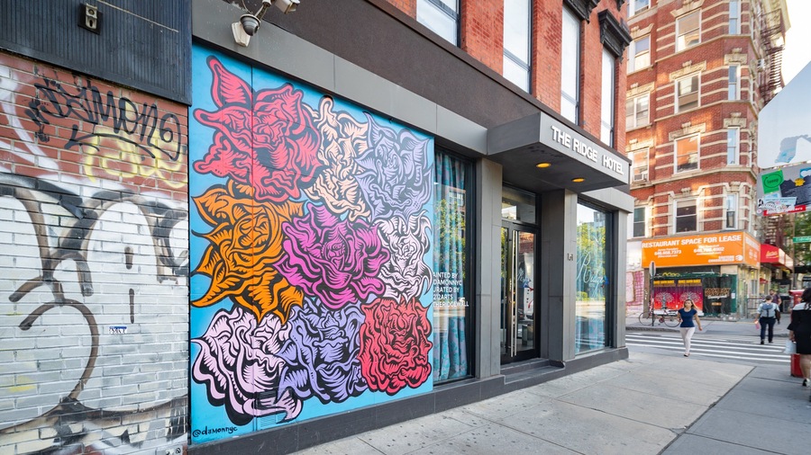 A colorful mural on a building's side, a hotel entrance, and a street with pedestrians.